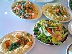 a table topped with white plates filled with different types of salads and dips