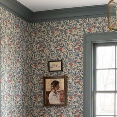 a painting hangs on the wall next to a window in a room with floral wallpaper