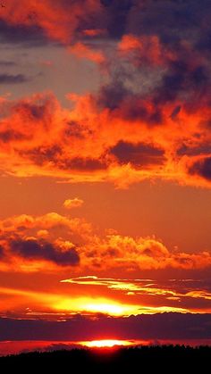 an airplane flying in the sky at sunset with clouds and trees around it, as the sun is setting