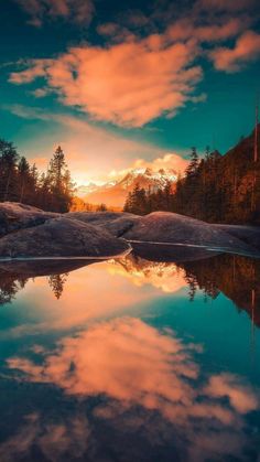 the sun is setting over a lake with mountains in the background and clouds reflected in the water