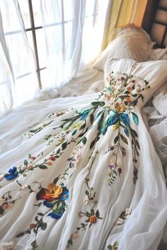 a dress is laying on top of a bed with white linens and flowers all over it