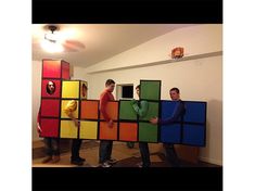 three men are standing in front of a colorful block wall that is made out of cardboard