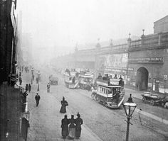 an old black and white photo of people walking down the street in front of buses