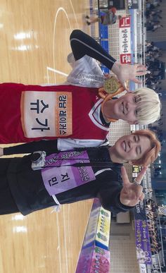 two women standing next to each other in front of a basketball court with signs on it