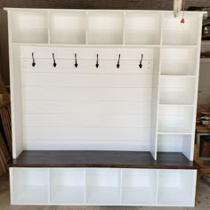 a white shelf with hooks on it next to a wall mounted coat rack and bench