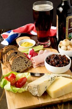 a wooden cutting board topped with cheese, meats and other foods next to bottles of beer