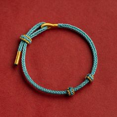 a blue and gold rope bracelet on a red surface with two yellow metal clasps