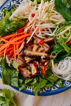 a blue and white plate topped with meat, veggies and noodle salad