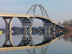 a bridge over water with trees in the background and blue sky reflected on the water