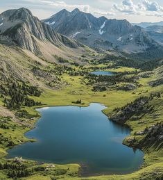 a lake in the middle of a mountain range surrounded by green grass and mountains with snow on them