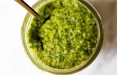 a jar filled with green pesto on top of a white countertop next to a wooden spoon