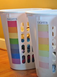 two white laundry baskets with different colored labels on the handles and sides, sitting on a wooden floor