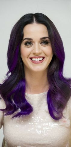 a woman with long purple hair smiling at the camera and wearing a white top,