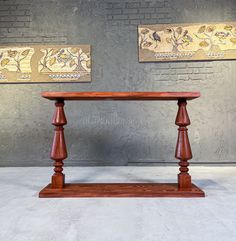 a wooden table with two paintings on the wall behind it