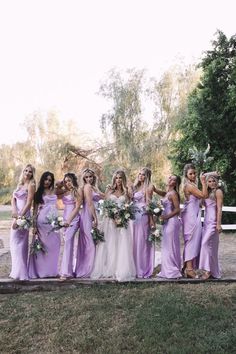 a group of women standing next to each other wearing purple dresses and holding bouquets