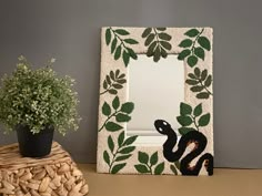 a decorative frame with a snake on it next to a potted plant