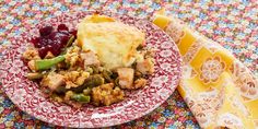 a red and white plate topped with food next to a yellow napkin on top of a colorful table cloth