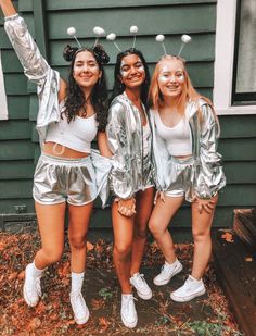 three girls in silver outfits posing for the camera with their arms up and one girl wearing white shoes