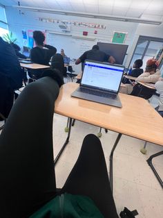 an open laptop computer sitting on top of a wooden table in front of people seated at desks