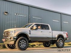 a white pickup truck parked in front of a building with large tires and rims