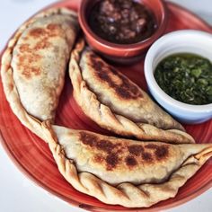 two pita breads on a red plate with dipping sauce in small bowls next to it