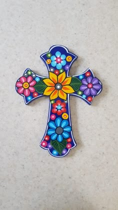 a colorful painted cross with flowers on the front and back side, sitting on a white surface