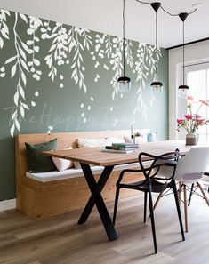 a dining room table with chairs and a bench in front of a wall that has leaves on it