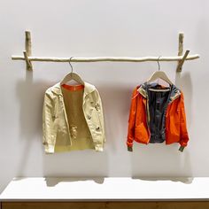 two jackets hanging on a clothes line in front of a white wall