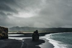 black sand beach with two large rocks sticking out of the water