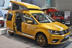 a yellow van is on display in a showroom with other cars behind it and an awning over the door