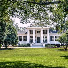 a large white house sitting in the middle of a lush green field next to trees