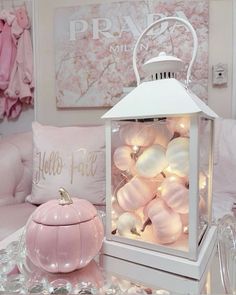 a white lantern sitting on top of a table next to a pink pumpkin and pillows