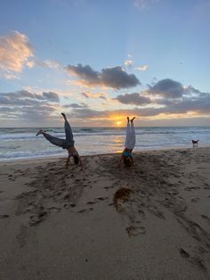 two people doing handstands on the beach at sunset