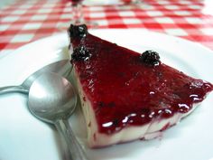 a piece of cheesecake on a white plate with spoons and red checkered table cloth