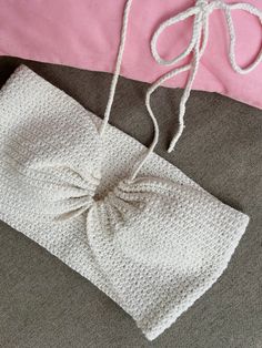 a white crocheted bag with a bow on it sitting next to a pink pillow