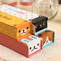 three colorful boxes with faces on them sitting on a doily next to a glass ball