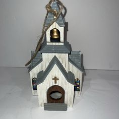 a small wooden church with a bell on it's roof and a rope hanging from the top