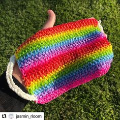 a hand is holding a colorful crocheted mitt in the middle of grass