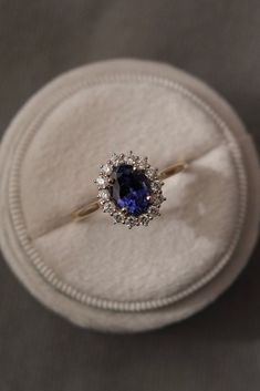 an engagement ring with a blue stone surrounded by white diamonds in a velvet box on a table