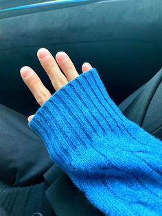 a person's hand wearing a blue knitted mitt sitting in the back seat of a car