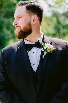 a man in a tuxedo looks off into the distance while wearing a boutonniere