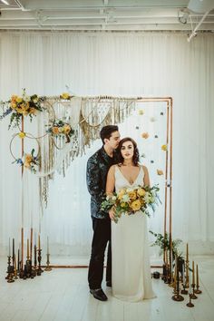 a man and woman standing next to each other in front of a wall with flowers