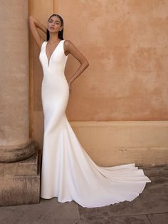 a woman standing next to a pillar wearing a white dress and posing for the camera