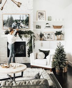 a woman is jumping in the air near a christmas tree and fireplace with pictures on the wall