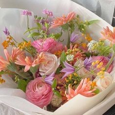 a bouquet of colorful flowers in a white paper bag on a table with other flowers