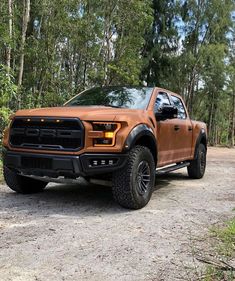 an orange truck is parked on the side of a dirt road in front of some trees