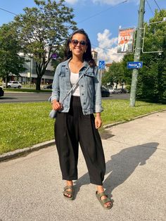 a woman is standing on the sidewalk in front of a street sign and some grass