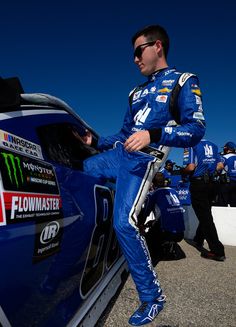 a man sitting on top of a blue car next to other men in the background