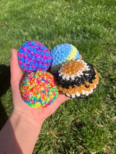 a hand is holding three colorful donuts in the grass