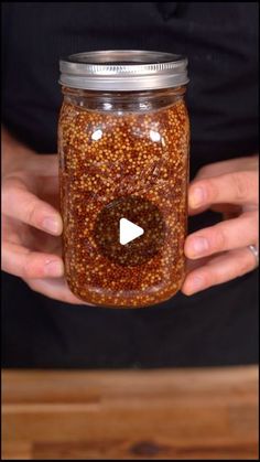 a person holding a jar filled with lots of brown stuff on top of a wooden table